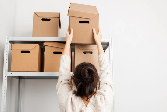 Person räumt Karton in Regal ein